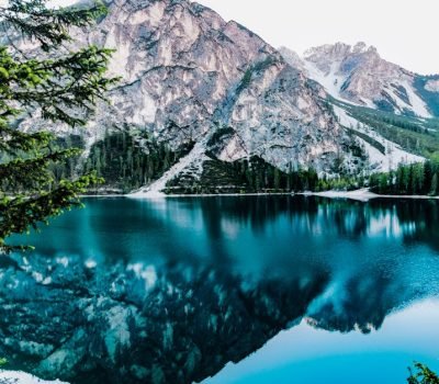 Serene mountain lake with stunning reflections in Braies, Italy, surrounded by trees.